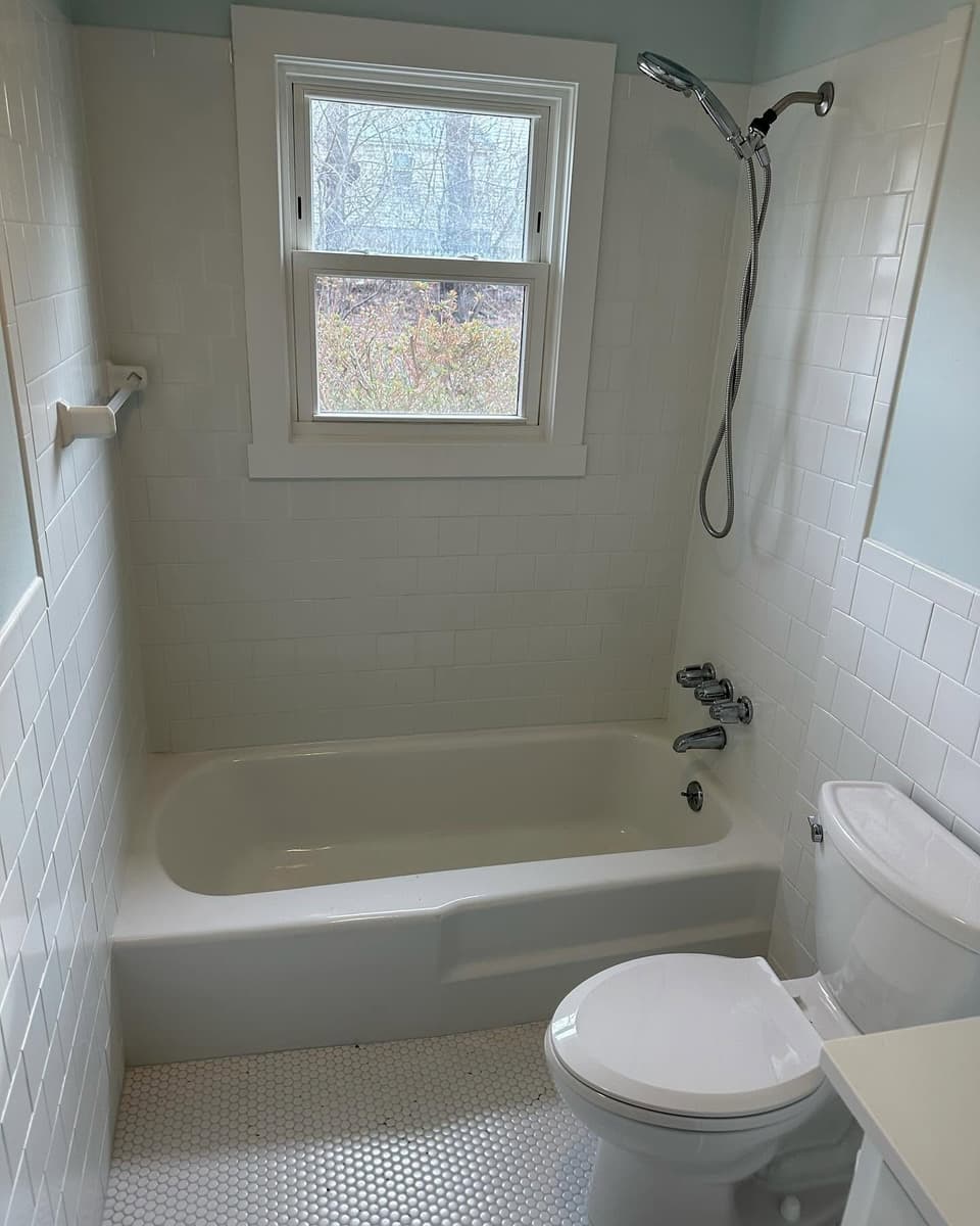 Finished bathroom by Farley Construction — white tiled tub surround and penny-round tile floor